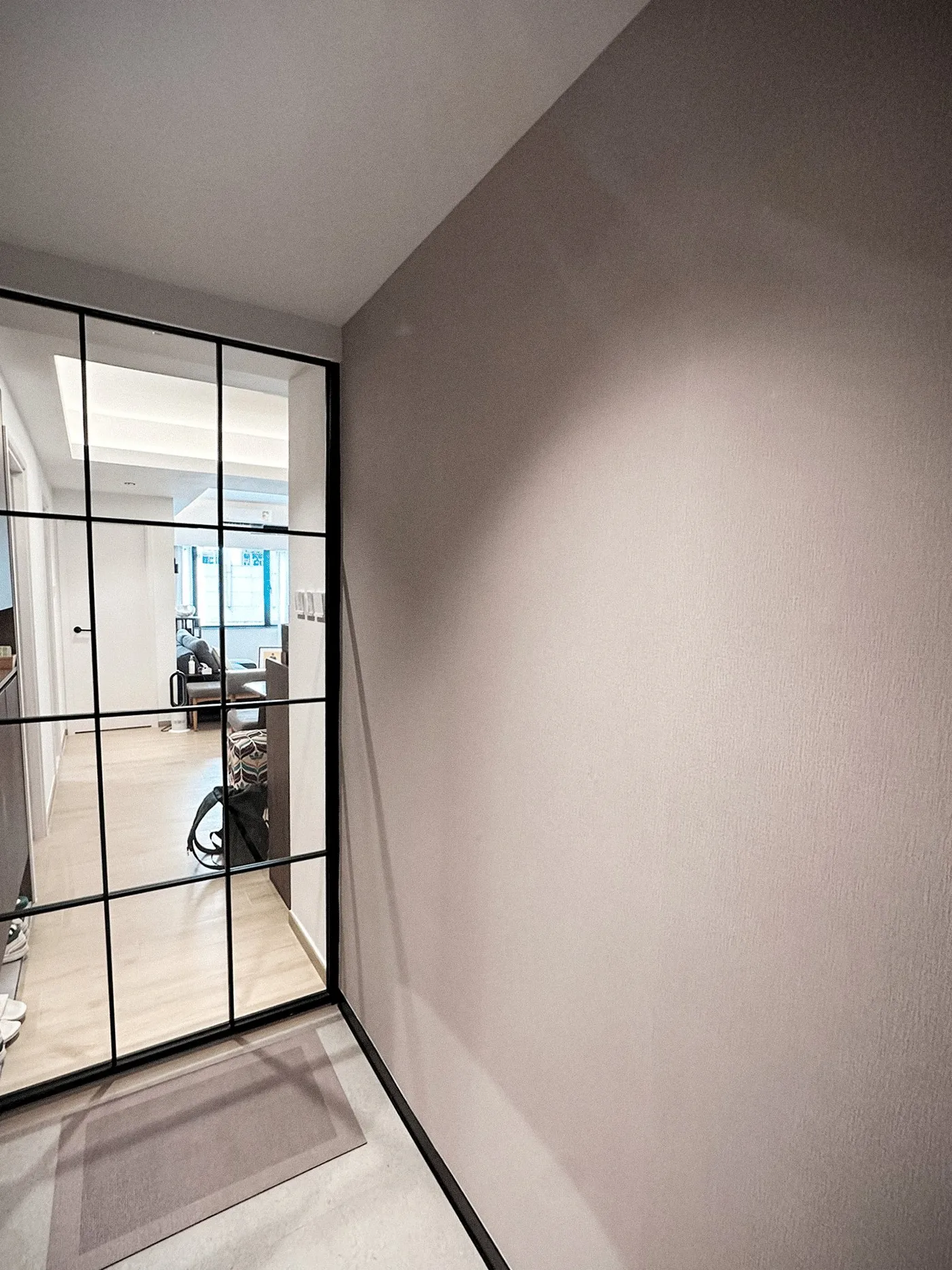 Entrance with a black-framed glass screen, a grey wall, a pale grey mat and a pale timber floor