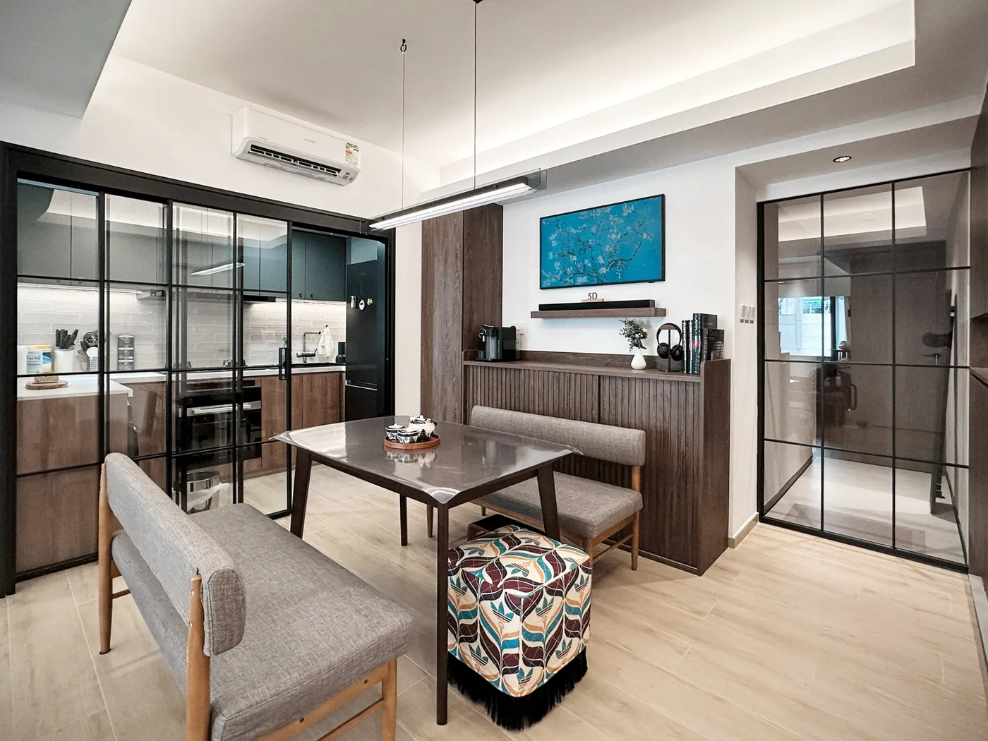 Dining area with a black-framed glass partition to the kitchen, a grey fabric banquette, a dark timber sideboard and blue artwork
