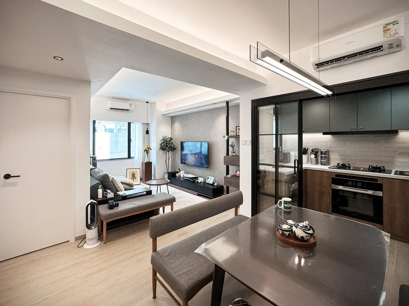 Living and dining areas joined, with grey fabric chairs, a dark table and a grey TV wall