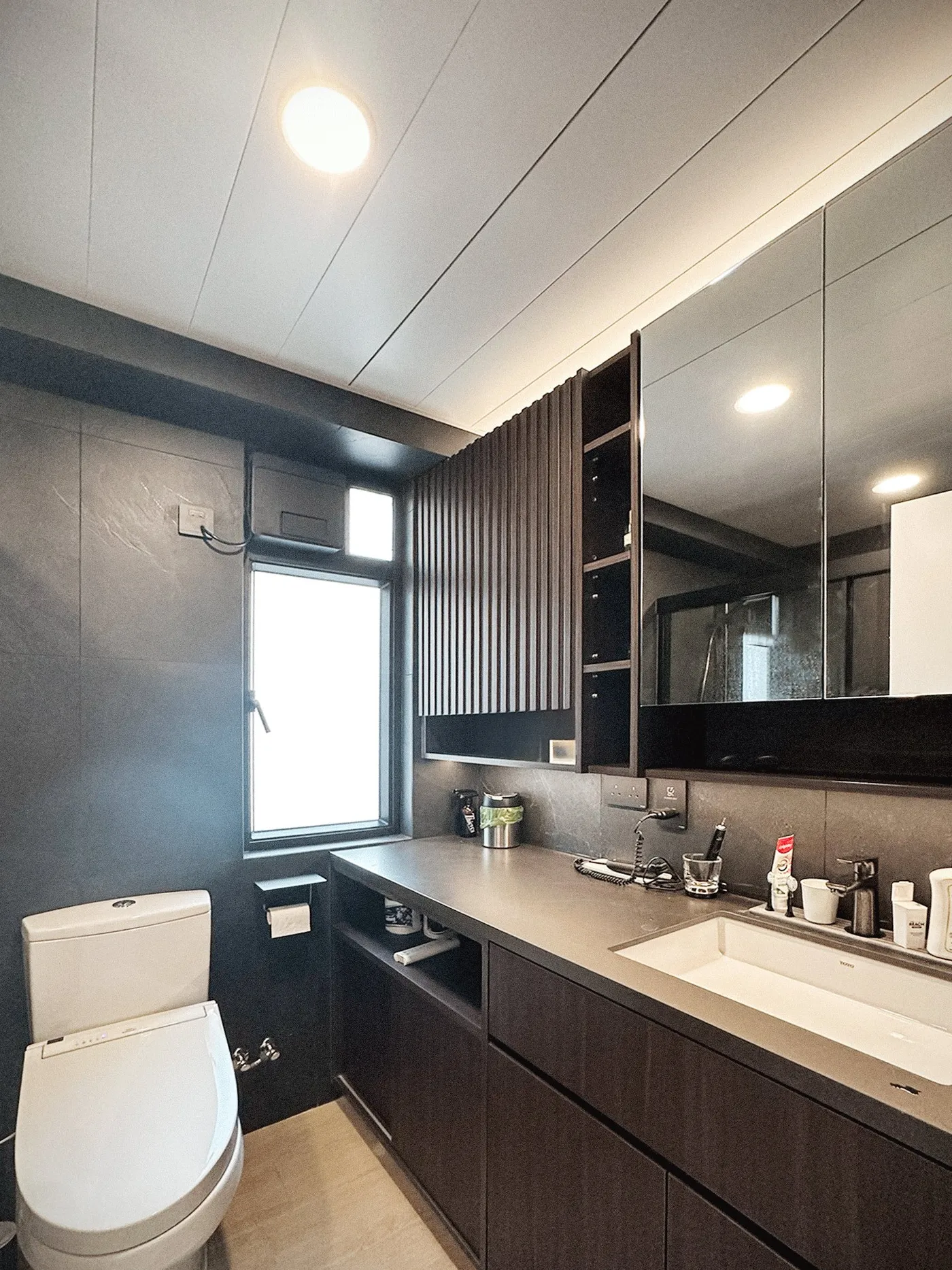 Bathroom vanity with grey stone-effect walls, a dark timber cabinet, a mirror cabinet and a white undermount basin