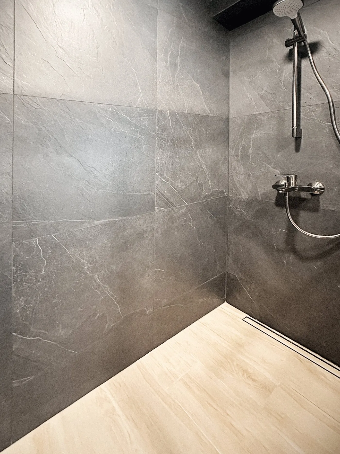Shower with grey stone-effect walls, a pale timber-effect floor and a stainless-steel shower