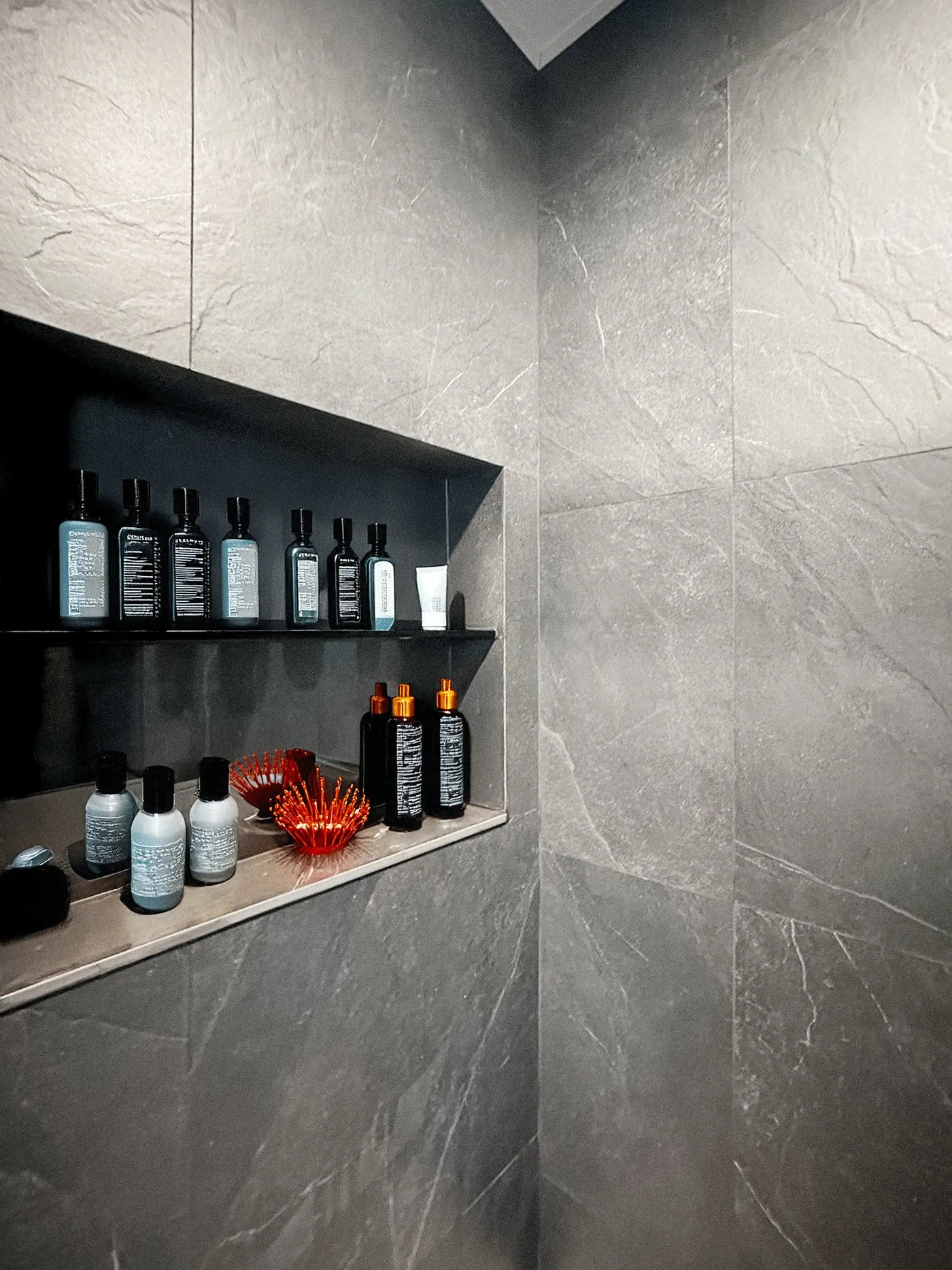 Bathroom wall niche in a grey stone-effect finish with shelves of toiletries