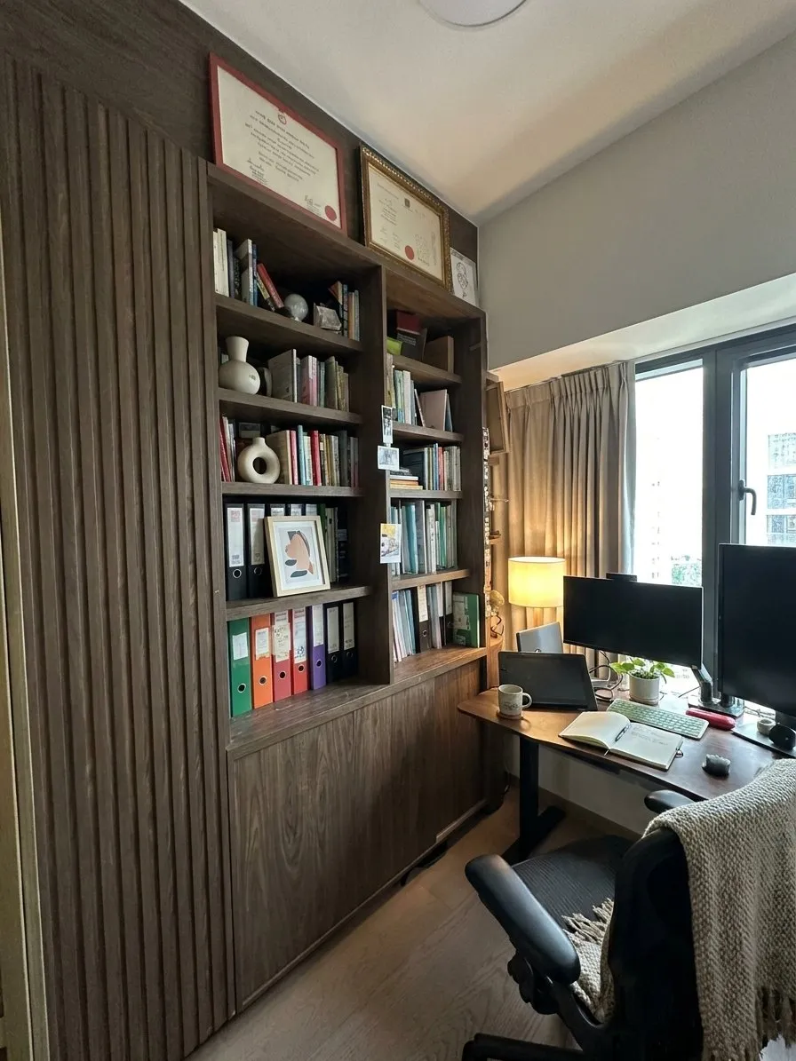書房木紋飾面書櫃連書檯，設開放式層架與玻璃吊櫃，檯面放有電腦螢幕及文件夾。