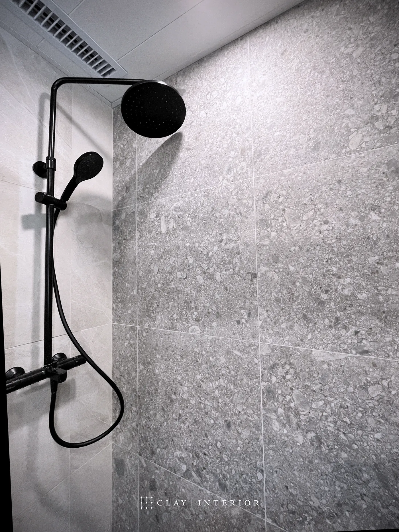 Bathroom shower area with black fittings and grey textured wall tiles