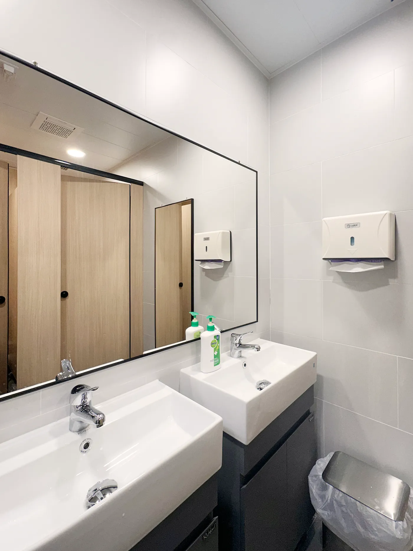 Washroom with a double vanity, black-framed mirrors, and light wood-grain partitions