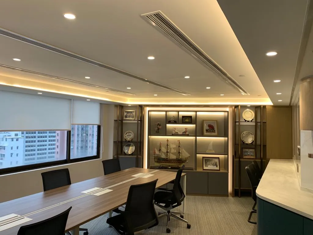 Meeting room with a long table and black office chairs, backlit display shelving and city views from the windows