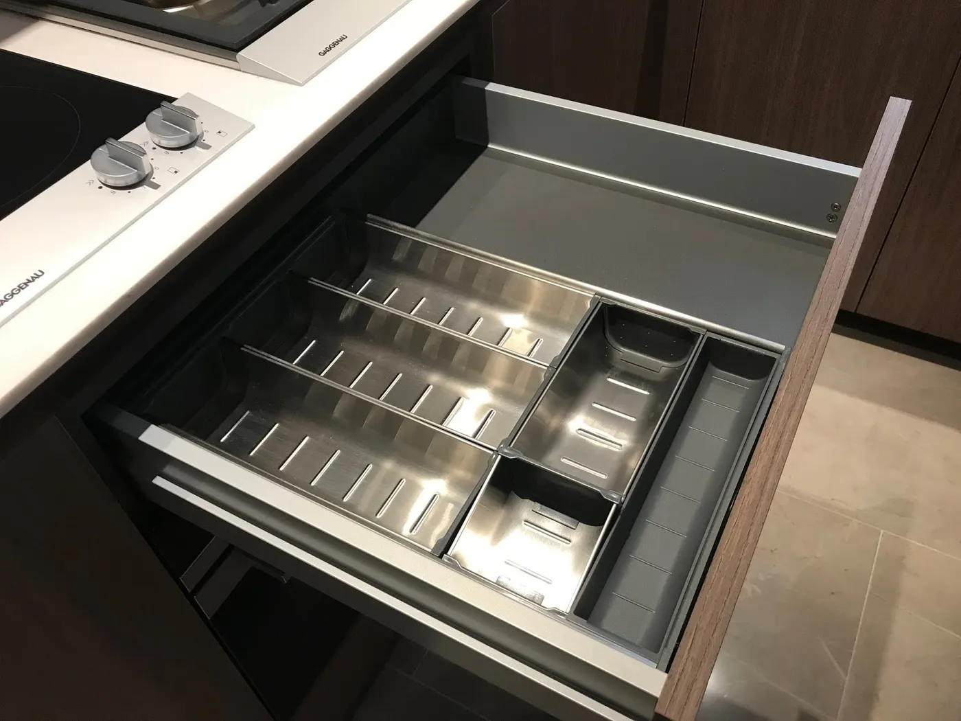 廚房抽屜內置不銹鋼餐具分格，木紋櫃身配白色檯面