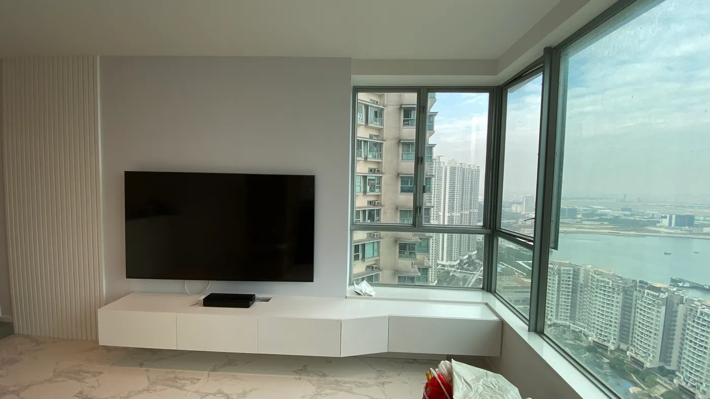 Floating TV cabinet running into the corner window, beside white fluted panelling, with a sea view