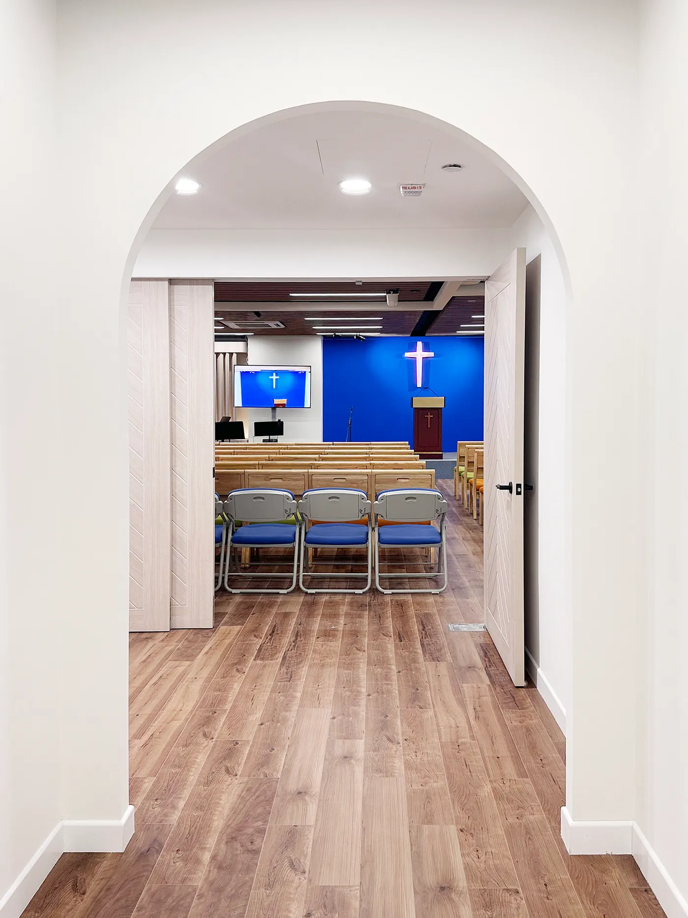 Arched corridor leading to the main hall, with a blue feature wall and illuminated cross