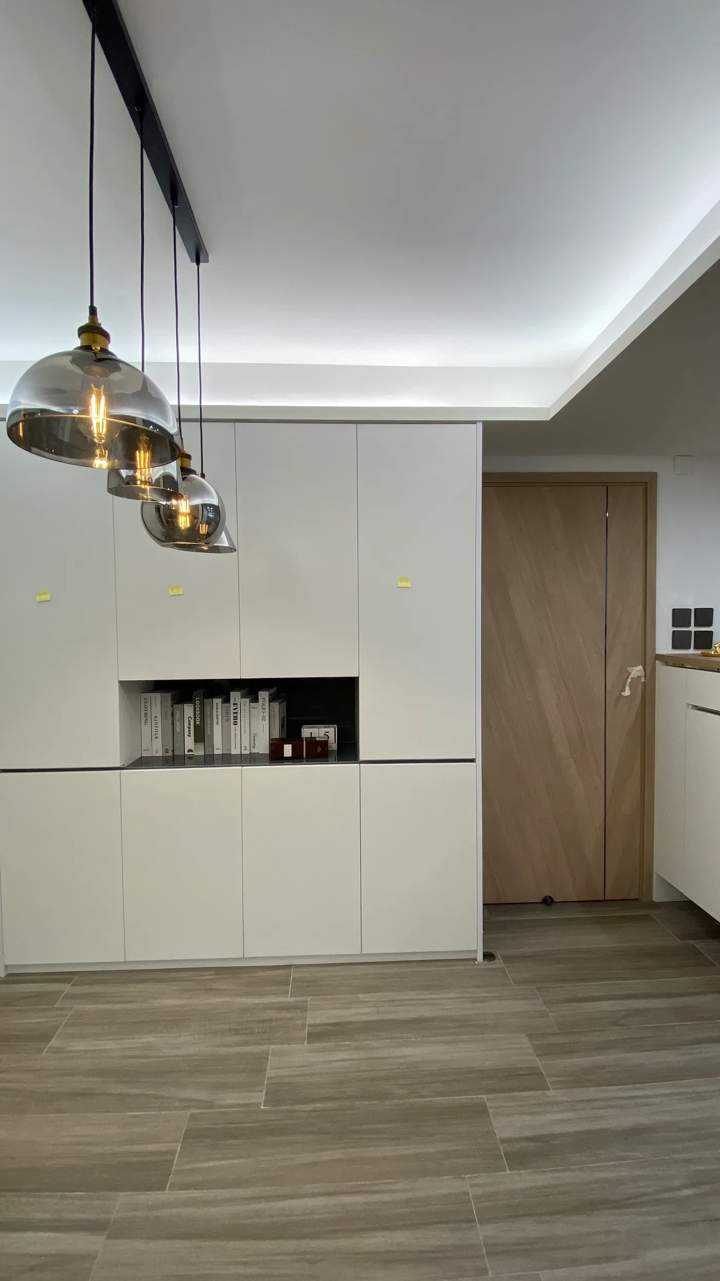 Full-height white storage wall in the dining area with a display niche, under smoked-glass pendants